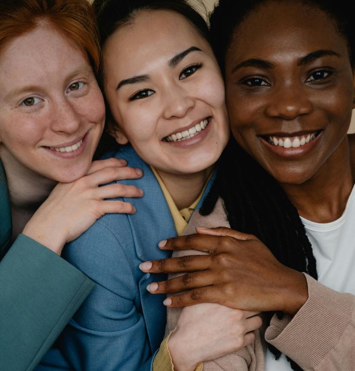 Three diverse women smiling and embracing, symbolizing friendship and unity.